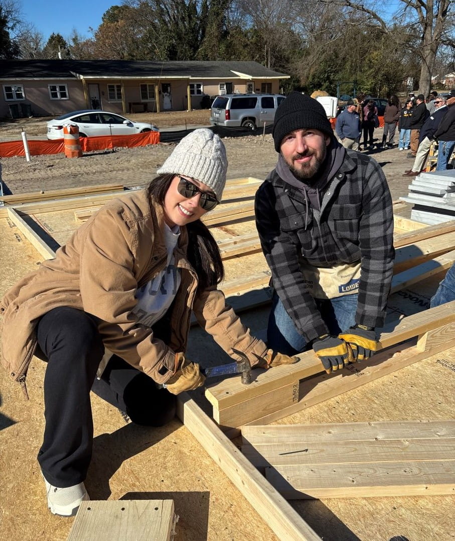 Two employee volunteers assembling wooden framing components at a Habitat for Humanity construction site.