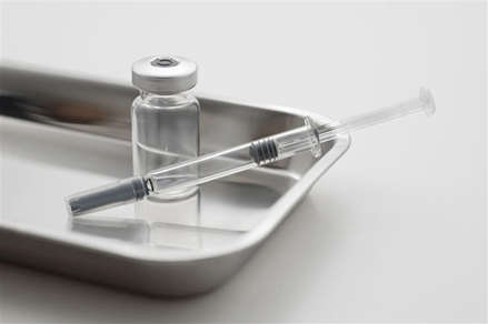Syringe and glass vial placed on a metal tray in a sterile setting.
