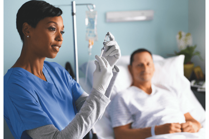 Nurse holding syringe and vial with patient in bed