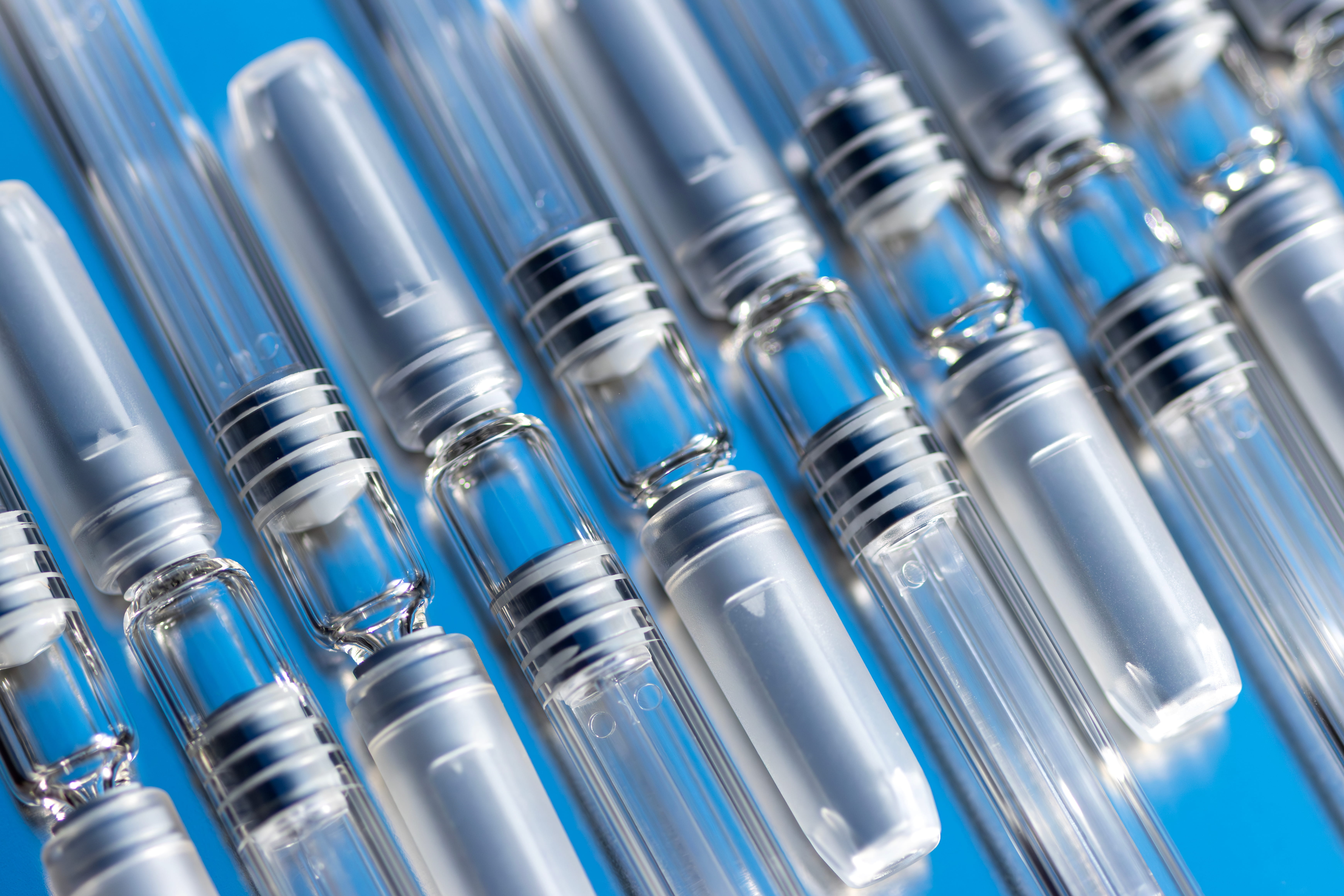 Close-up of rows of empty glass prefillable syringes with white plungers.