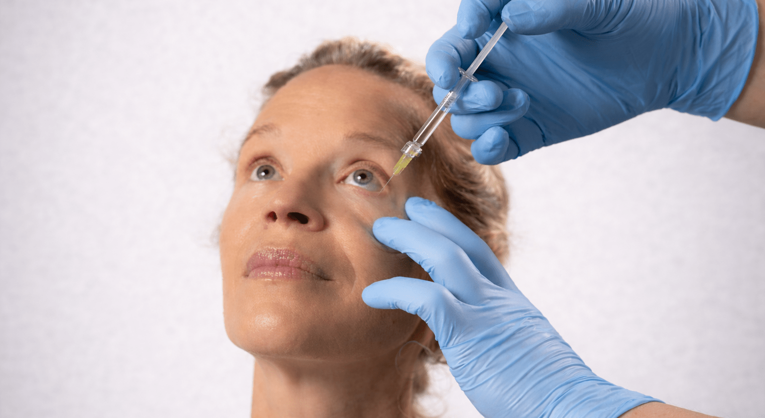 Intravitreal eye injection being administered by a clinician wearing blue gloves.